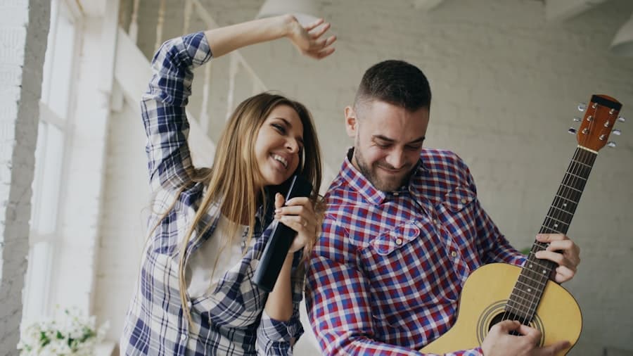 Two friends laughing while singing and playing guitar together at home